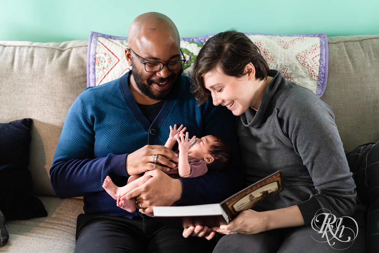 Black man and woman read to their newborn baby on the couch at home in Saint Paul, Minnesota.