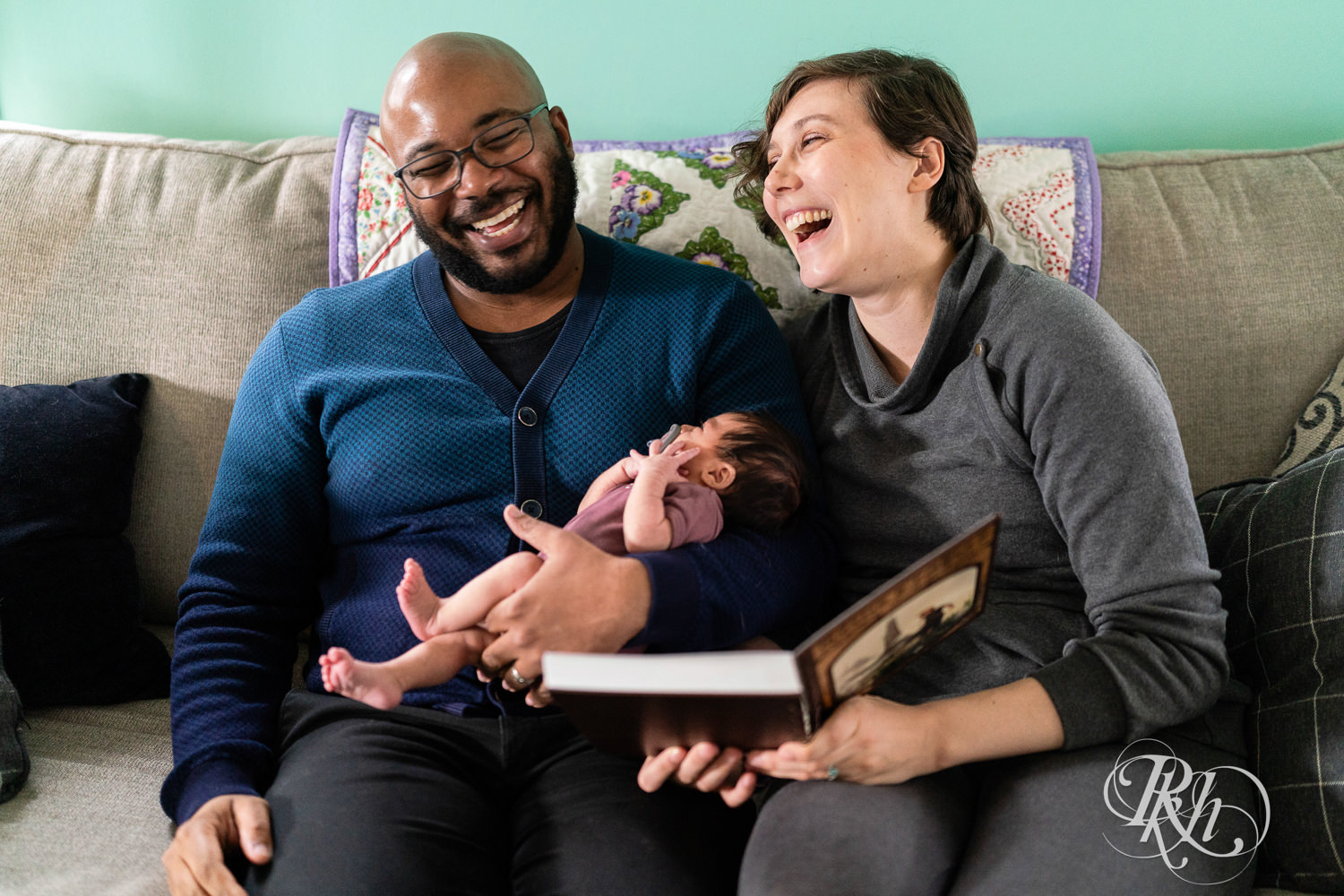 Black man and woman read to their newborn baby on the couch at home in Saint Paul, Minnesota.