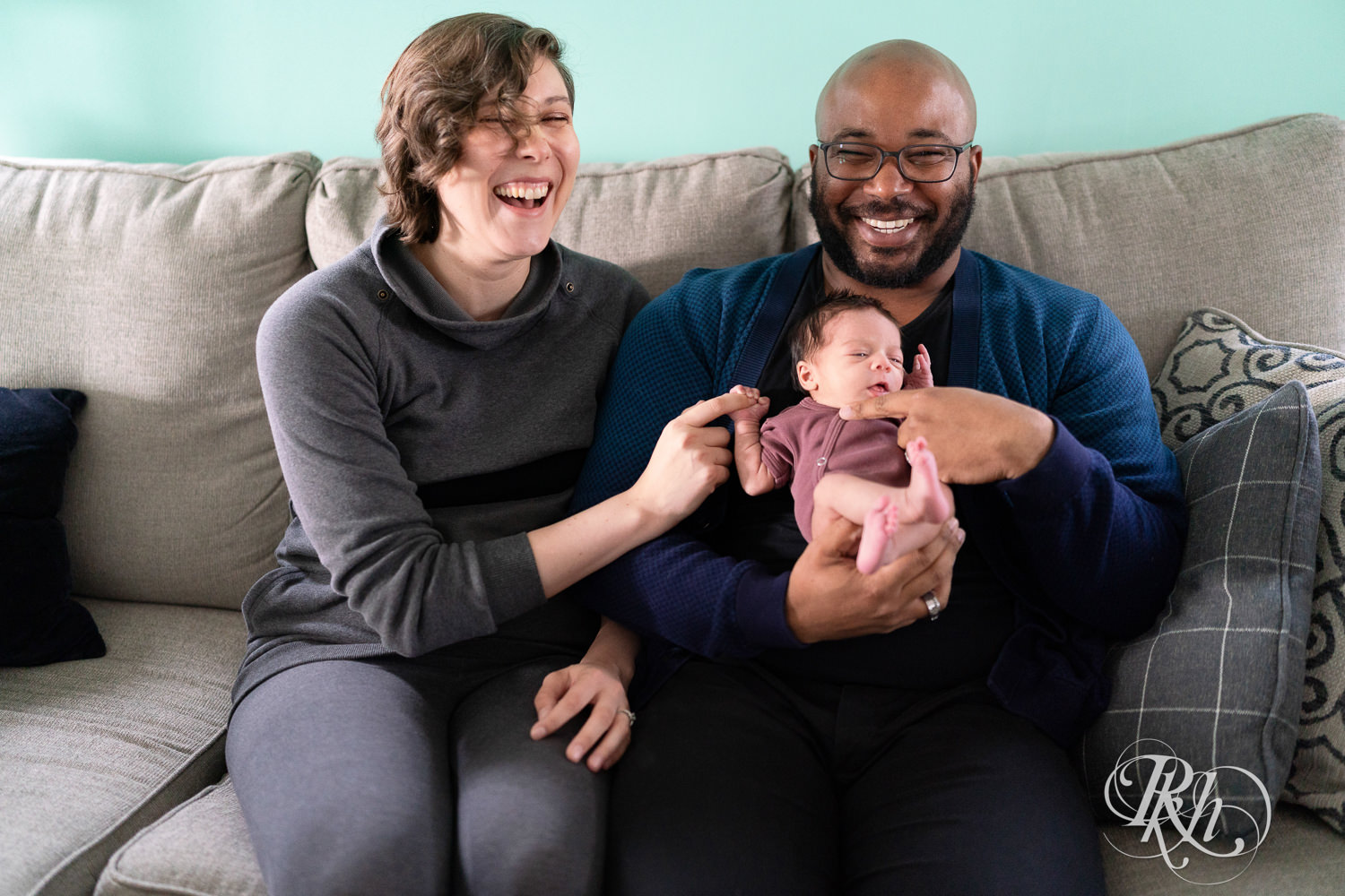 Black man and woman laugh on couch with newborn baby at home in Saint Paul, Minnesota.