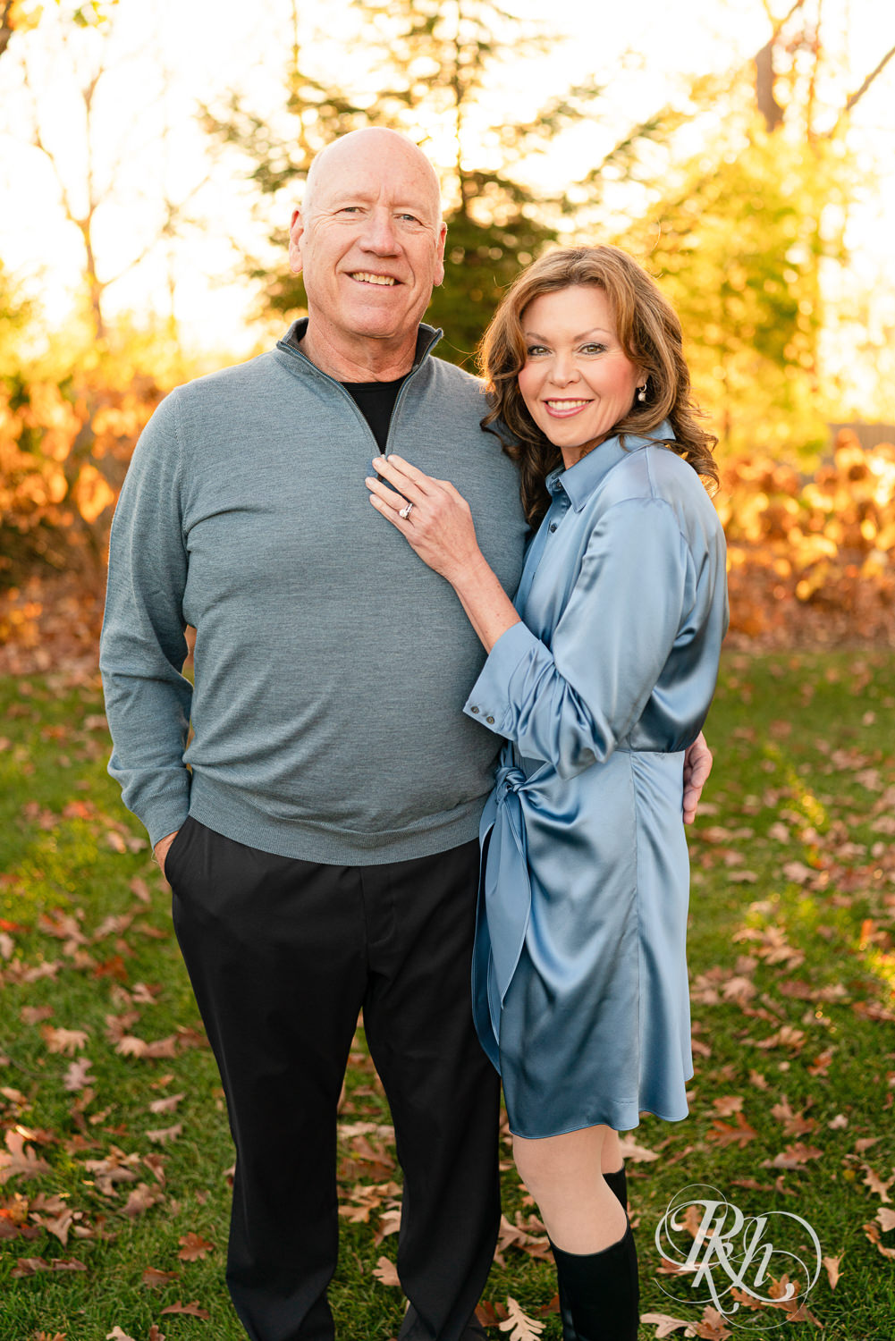 Man in blue shirt and black pants and woman in blue dress smile during sunset family photos in Wayzata, Minnesota.
