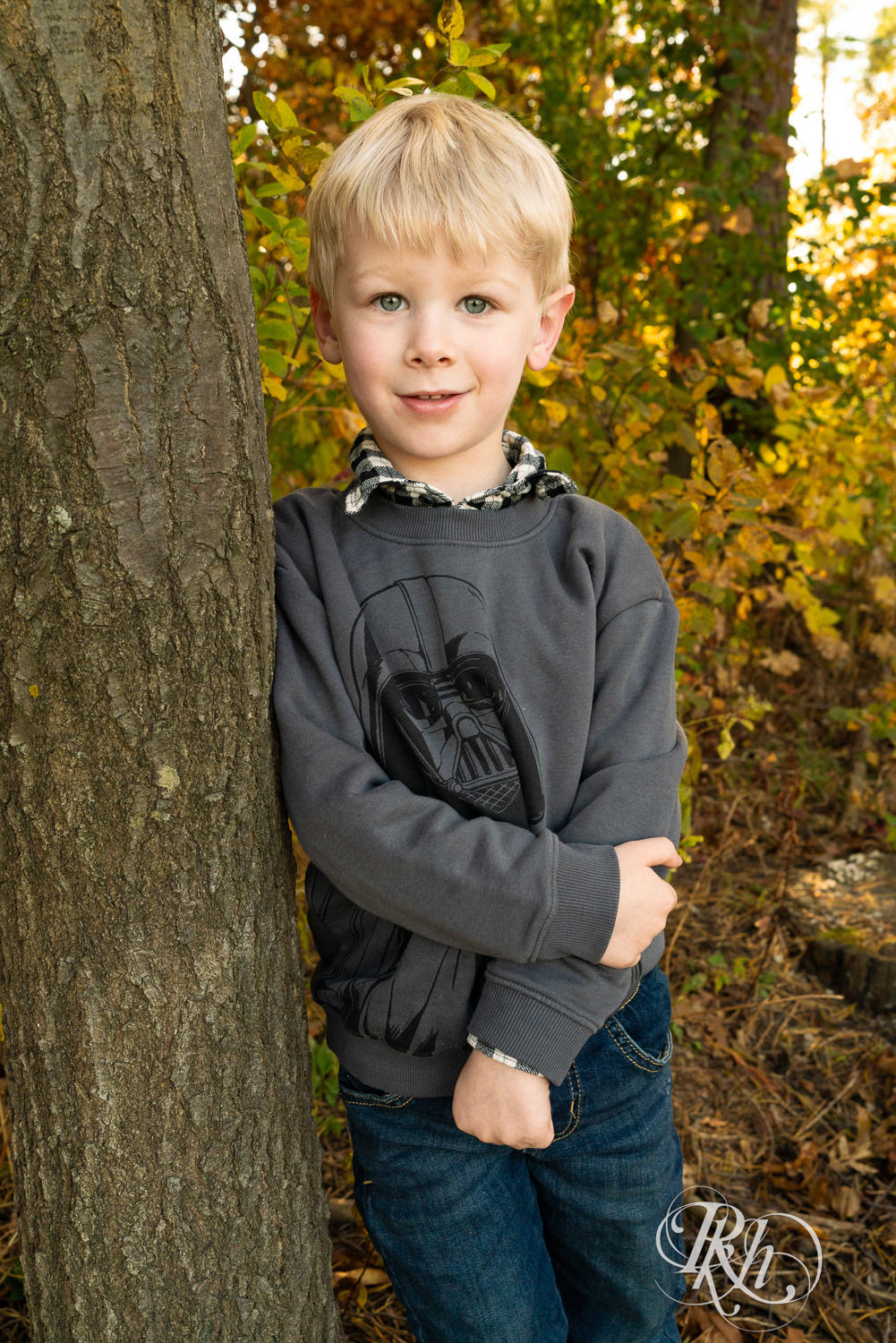 Little blond boy in Darth Vader shirt smiles during fall morning family photos in Lebanon Hills Regional Park in Eagan, Minnesota.