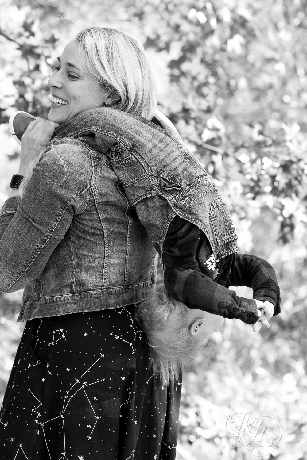 Little blond boy smiles on mom's back in Lebanon Hills Regional Park in Eagan, Minnesota.