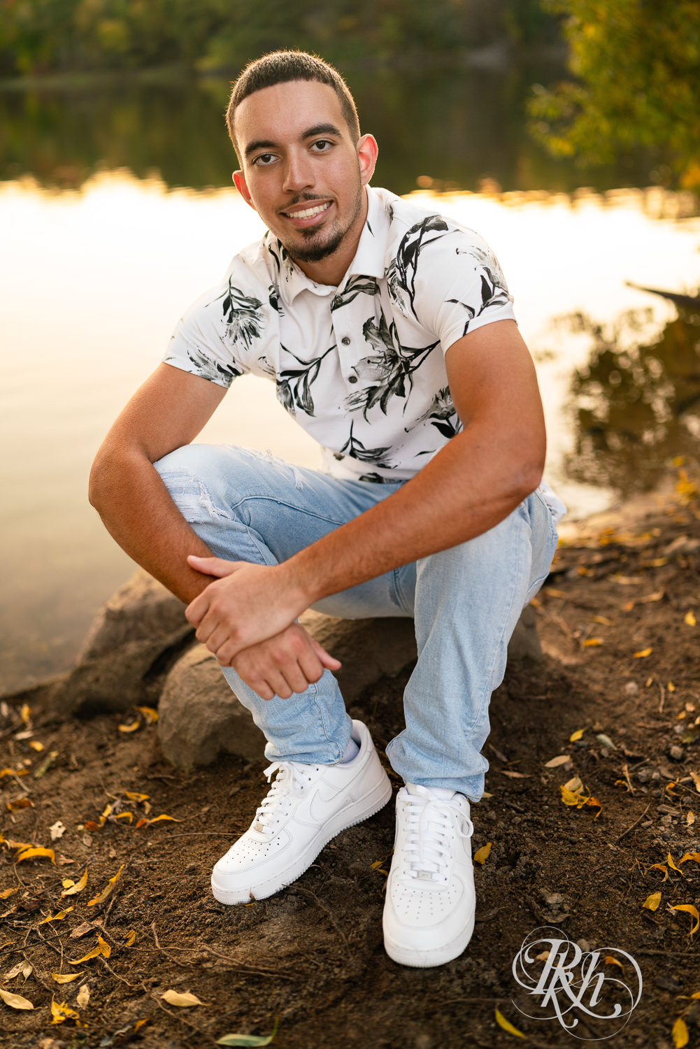 Black senior boy smiles in front of lake during sunset in Eagan, Minnesota.