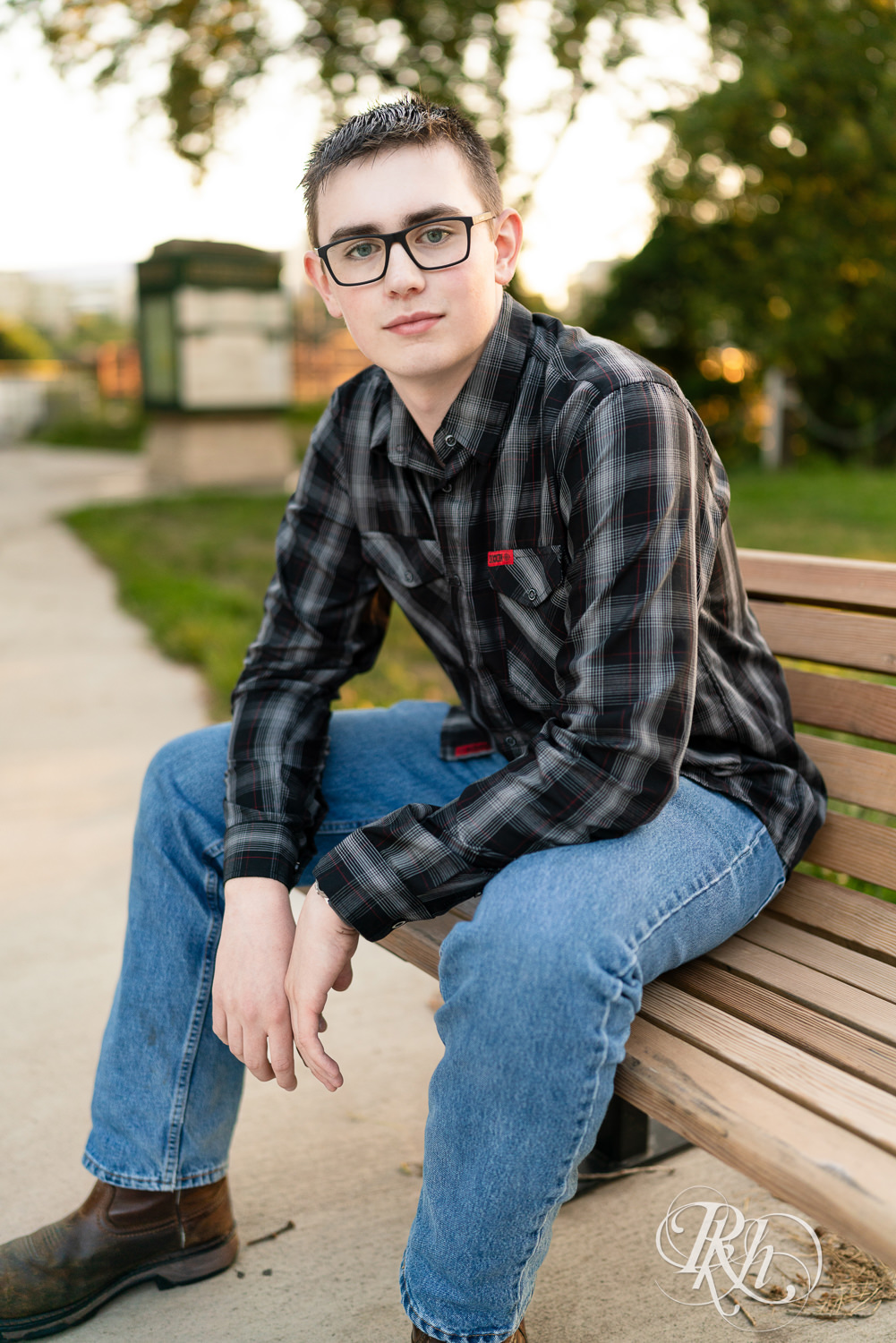 Senior boy wearing glasses and a flannel sits on a bench in Minneapolis, Minnesota.