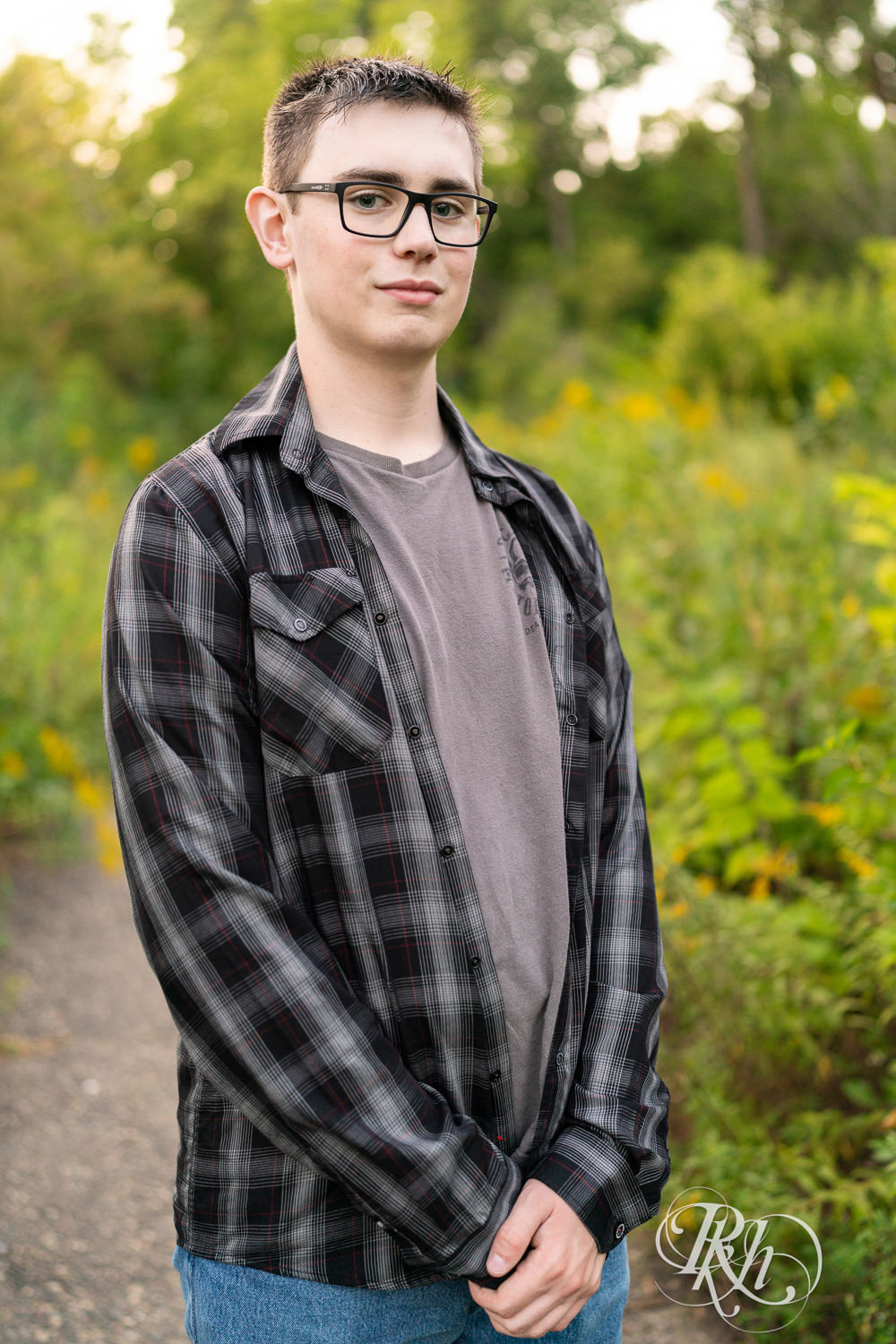 Senior boy wearing glasses and a flannel smiles in a field during sunset in Minneapolis, Minnesota.