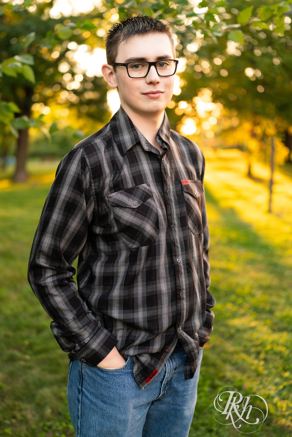 Senior boy wearing glasses and a flannel smiles during sunset senior photography in Minneapolis, Minnesota.