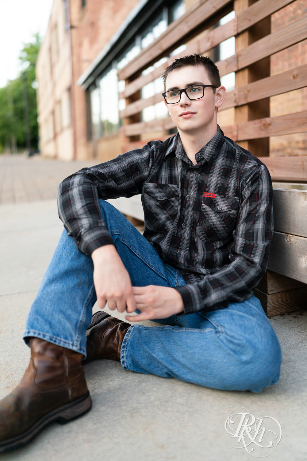 Senior boy wearing glasses and a flannel sits on the sidewalk during senior session in Minneapolis, Minnesota.