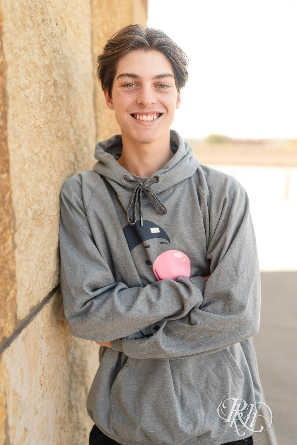 Senior boy in sweatshirt smiles in front of Target Field in Minneapolis, Minnesota.