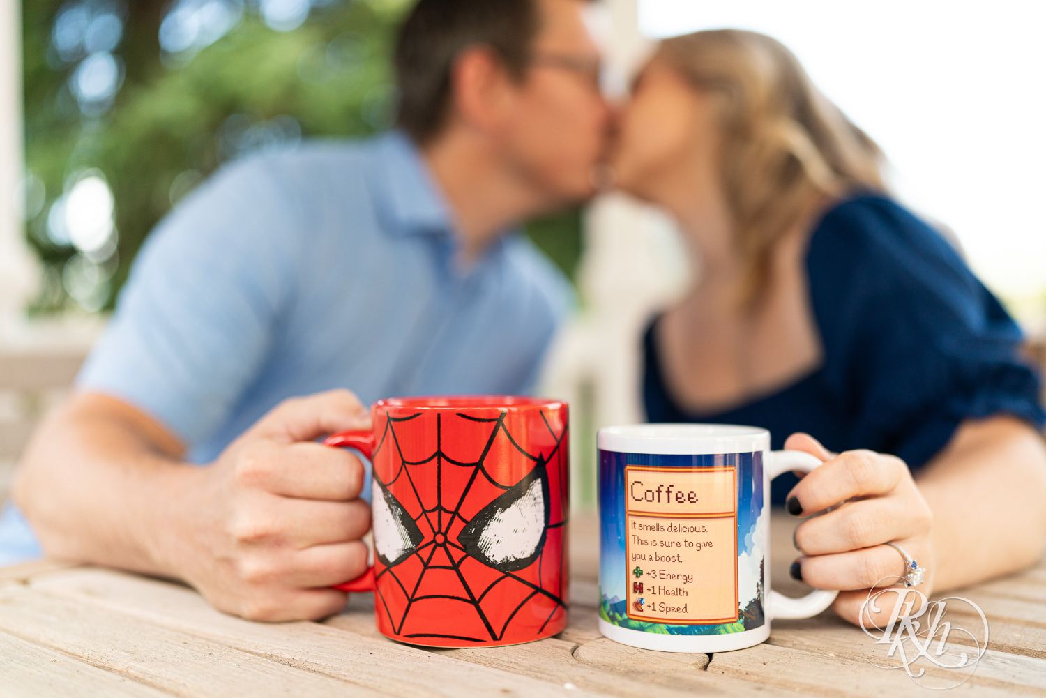 Man and woman in blue dress kiss while holding coffee cups at Centennial Lakes Park in Edina, Minnesota.