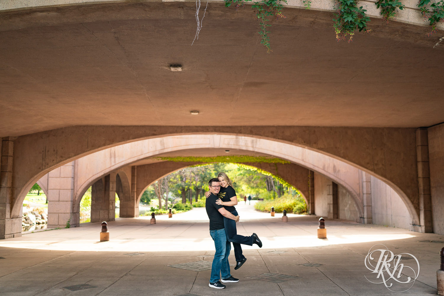 Man lifts woman in Zelda shirt under bridge at Centennial Lakes Park in Edina, Minnesota.