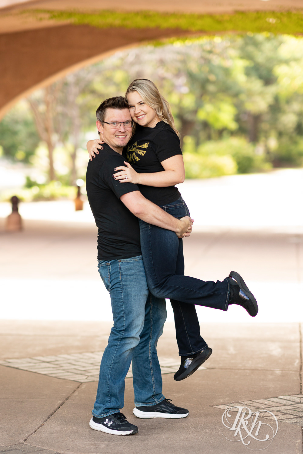 Man lifts woman in Zelda shirt under bridge at Centennial Lakes Park in Edina, Minnesota.