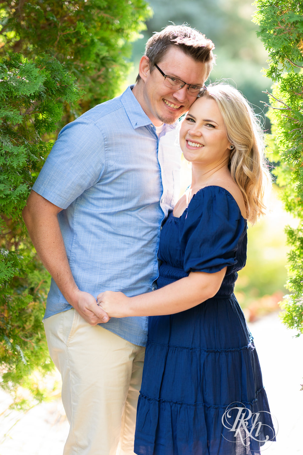 Man and woman in blue dress smile during morning engagement photography at Centennial Lakes Park in Edina, Minnesota.