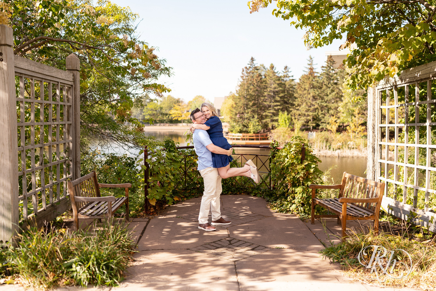 Man lifts woman in blue dress in front of the lake at Centennial Lakes Park in Edina, Minnesota.