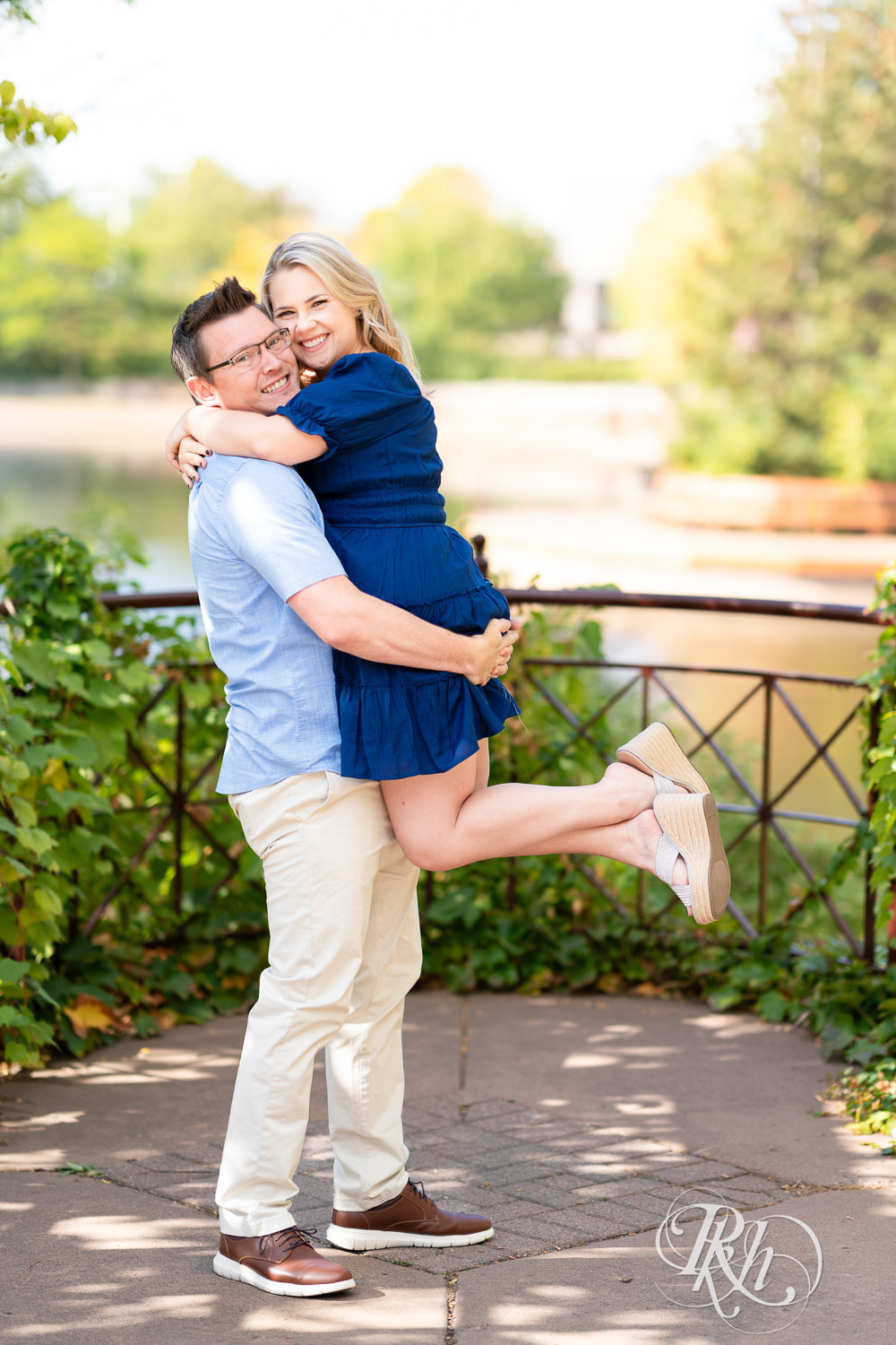 Man lifts woman in blue dress in front of the lake at Centennial Lakes Park in Edina, Minnesota.