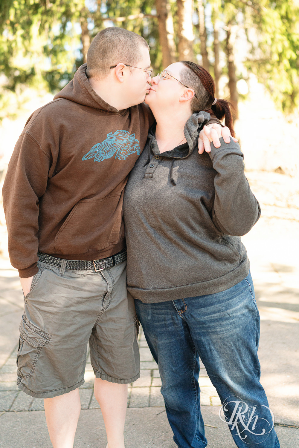 Man and woman in sweatshirts kiss during engagement photography at Centennial Lakes Park in Edina, Minnesota.