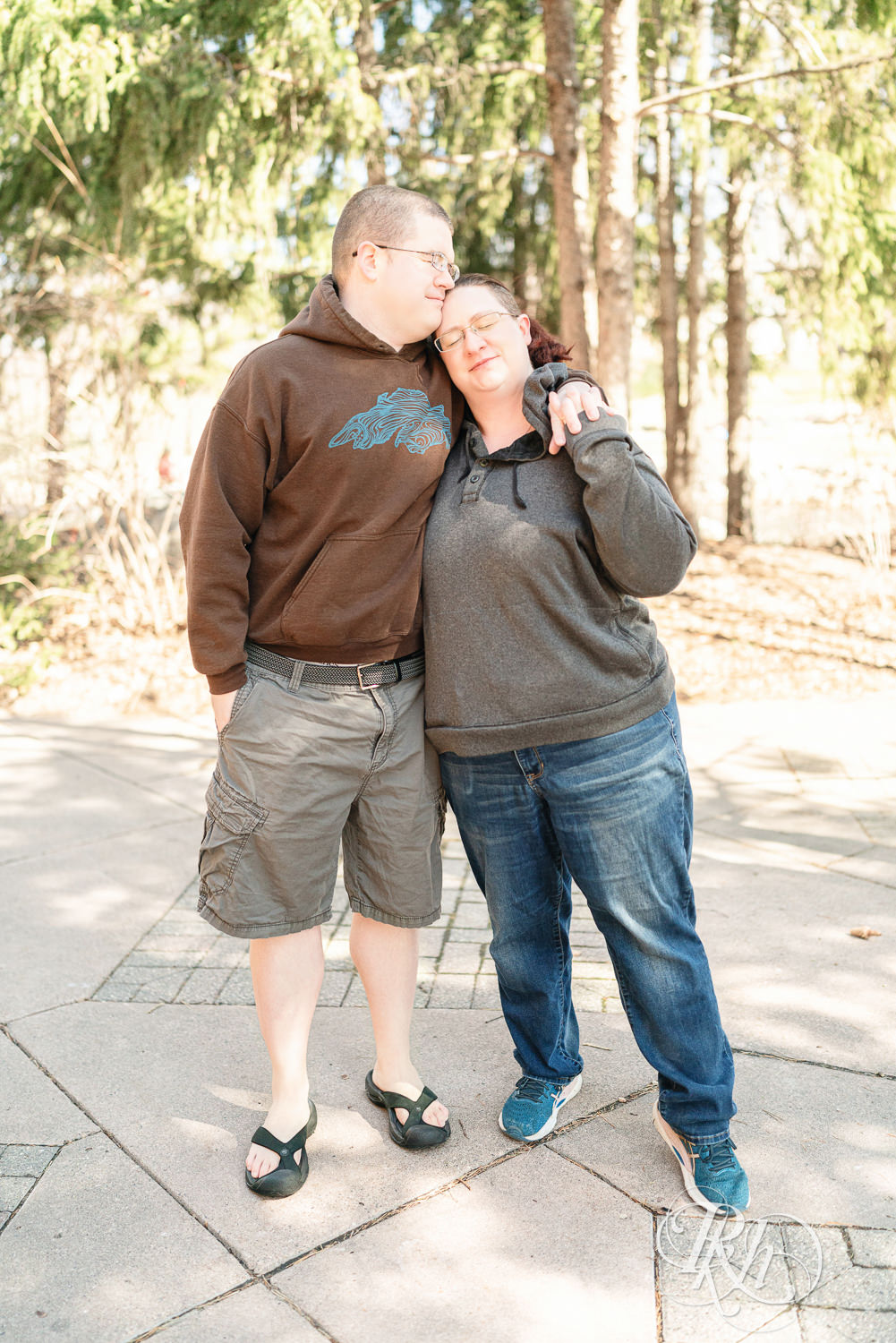 Man and woman in sweatshirts snuggle during engagement photography at Centennial Lakes Park in Edina, Minnesota.