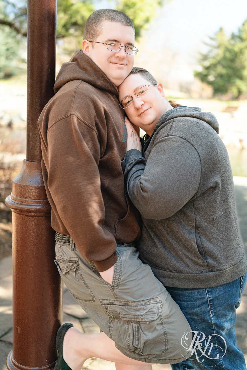 Man and woman in sweatshirts smile during engagement photography at Centennial Lakes Park in Edina, Minnesota.