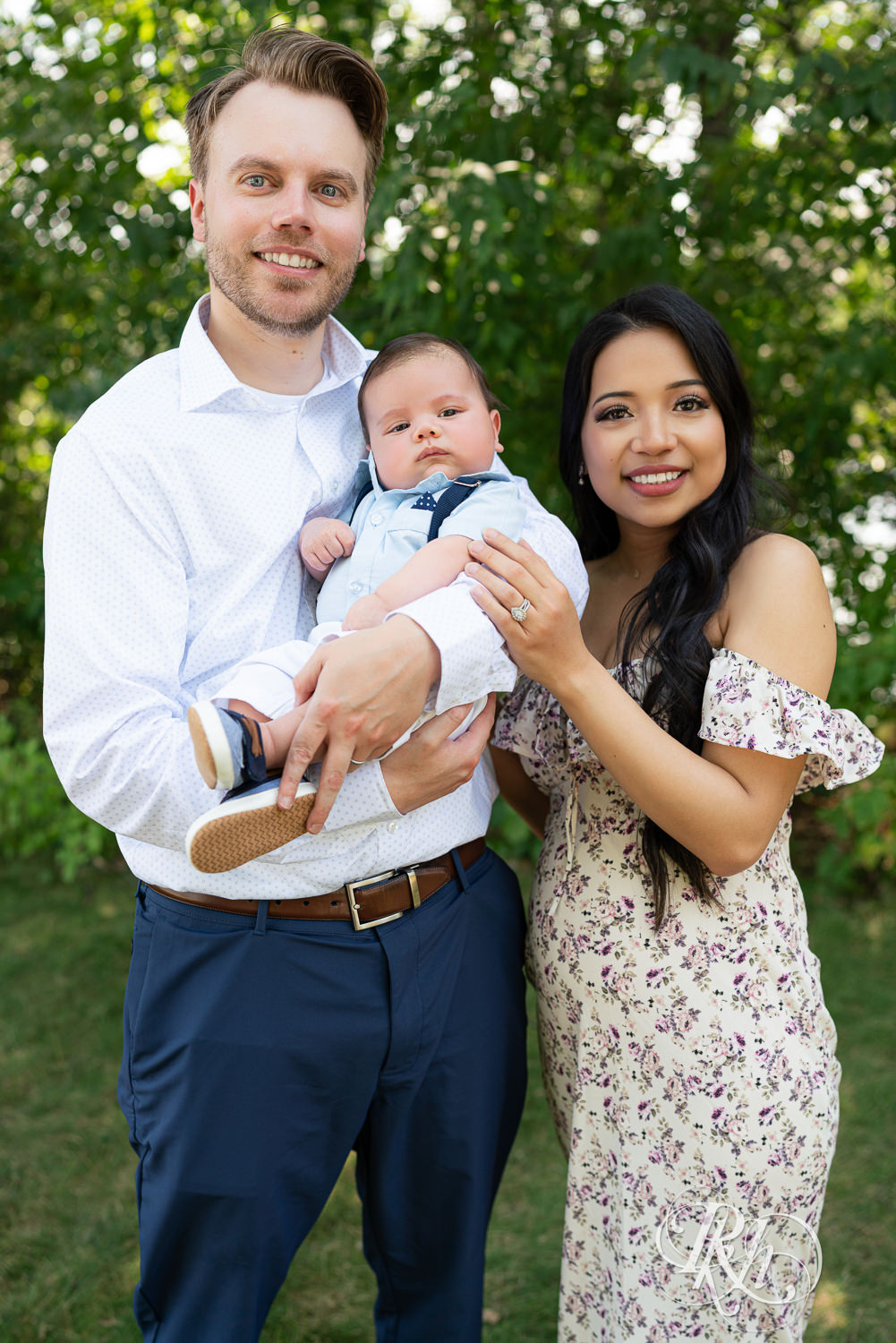 Woman in floral dress and man in dress shirt and pants smile with their baby at Lebanon Hills Regional Park in Eagan, Minnesota.