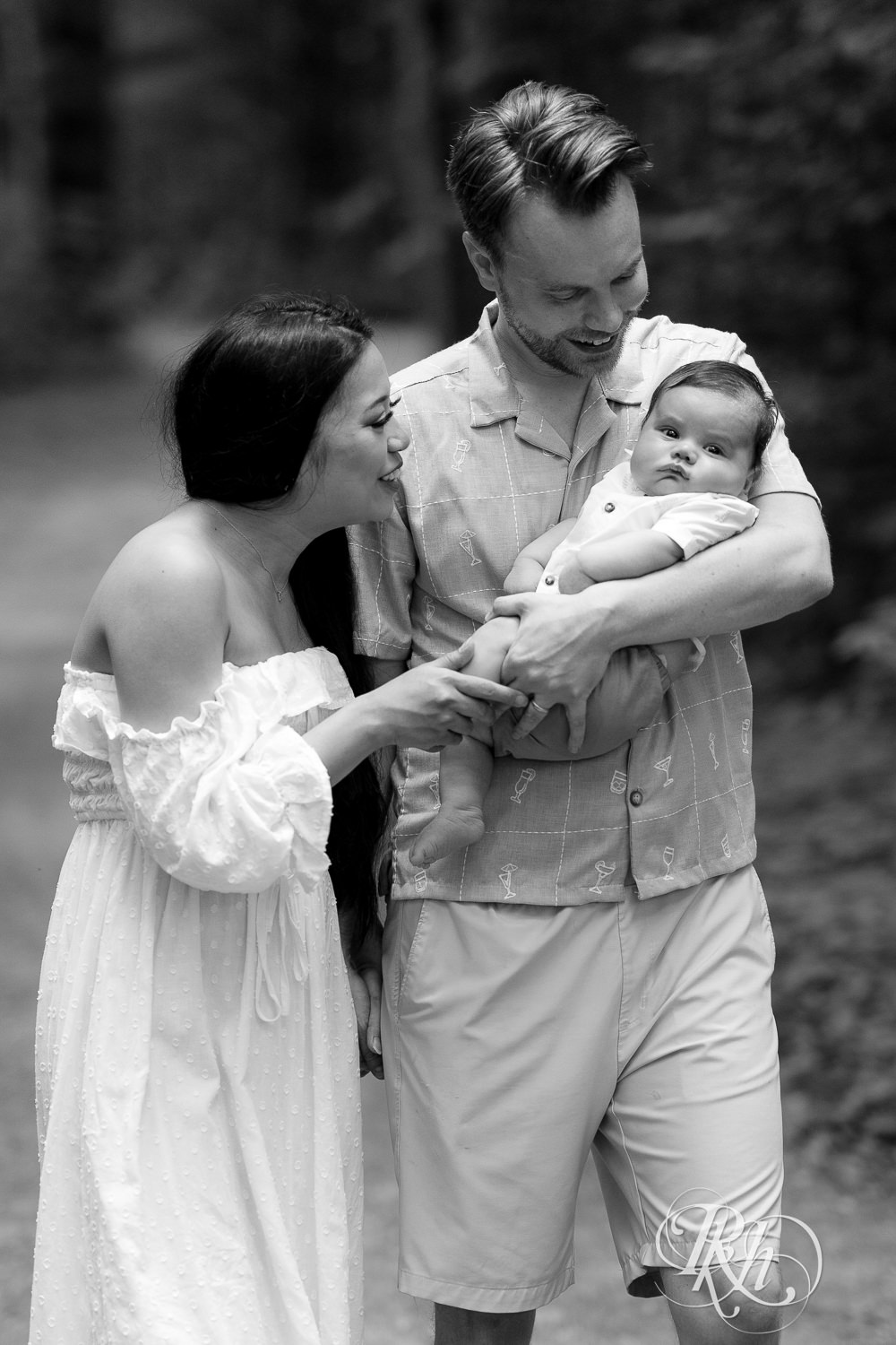 Woman in white dress and man in green dress shirt and shorts walk down a trail holding their baby at Lebanon Hills Regional Park in Eagan, Minnesota.