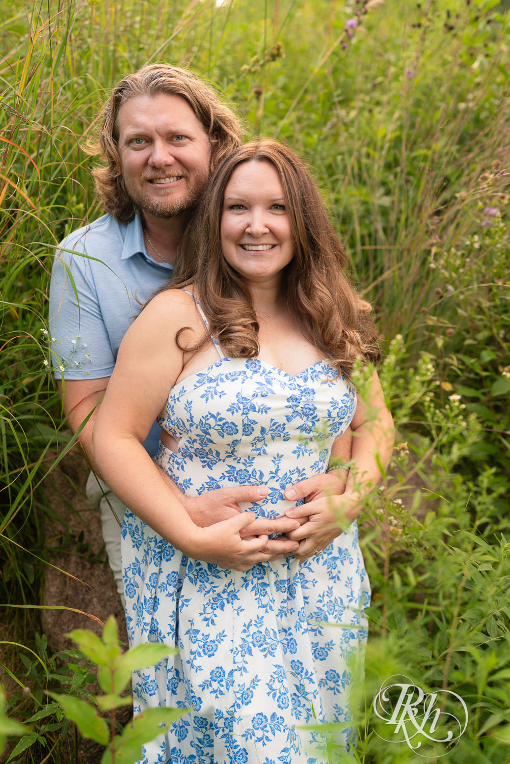 Man in blue shirt and khaki shorts and woman in blue and white dress smile within flowers in Eagan, Minnesota.