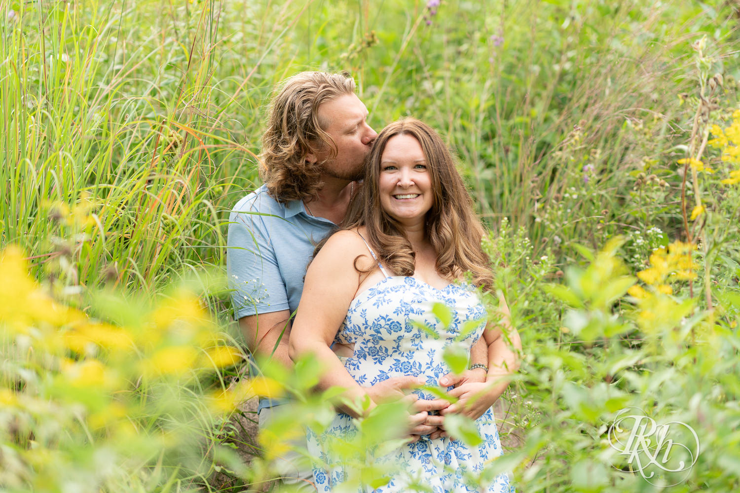 Man in blue shirt and khaki shorts and woman in blue and white dress smile within flowers in Eagan, Minnesota.