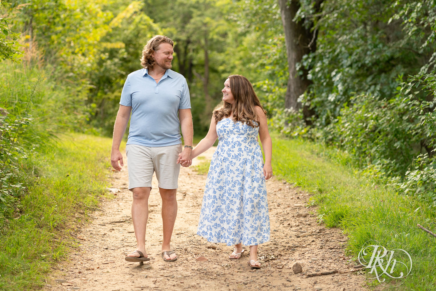 Man in blue shirt and khaki shorts and woman in blue and white dress walk down a trail in Eagan, Minnesota.