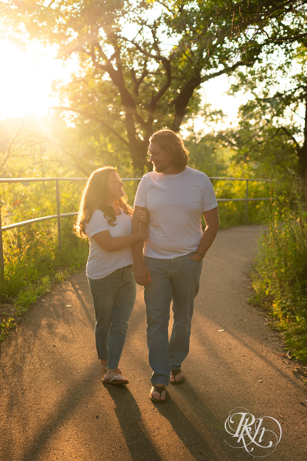 Man and woman dressed in white t-shirts and jeans walk down a path at sunset in Eagan, Minnesota.