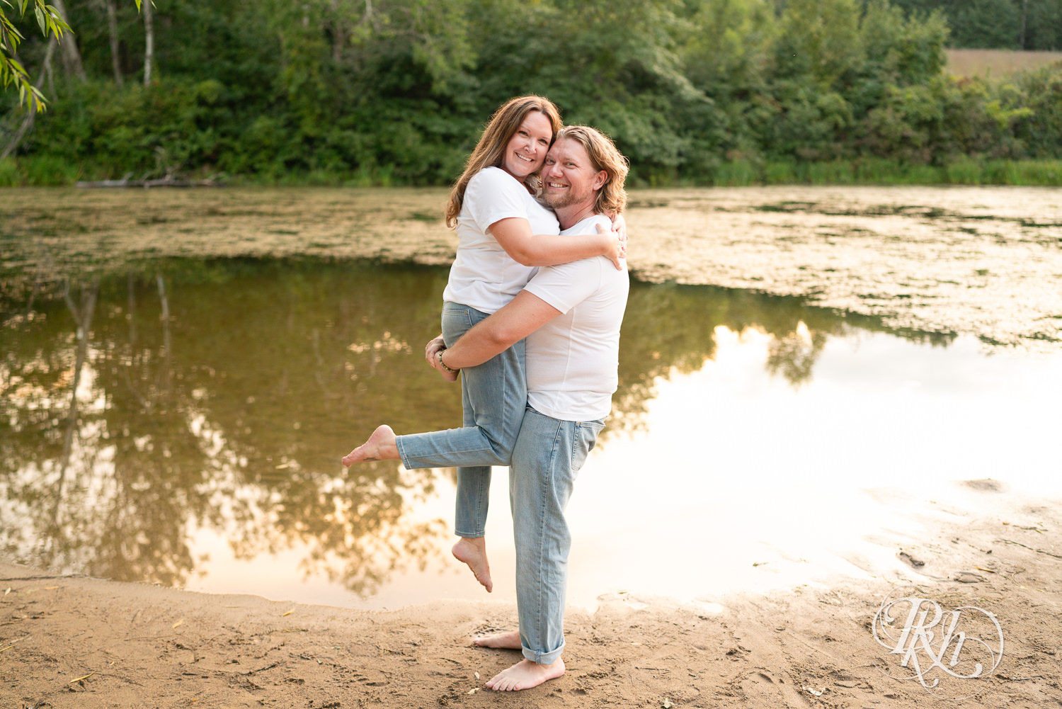 Man and woman dressed in white t-shirts and jeans smile on the beach at sunset in Eagan, Minnesota.