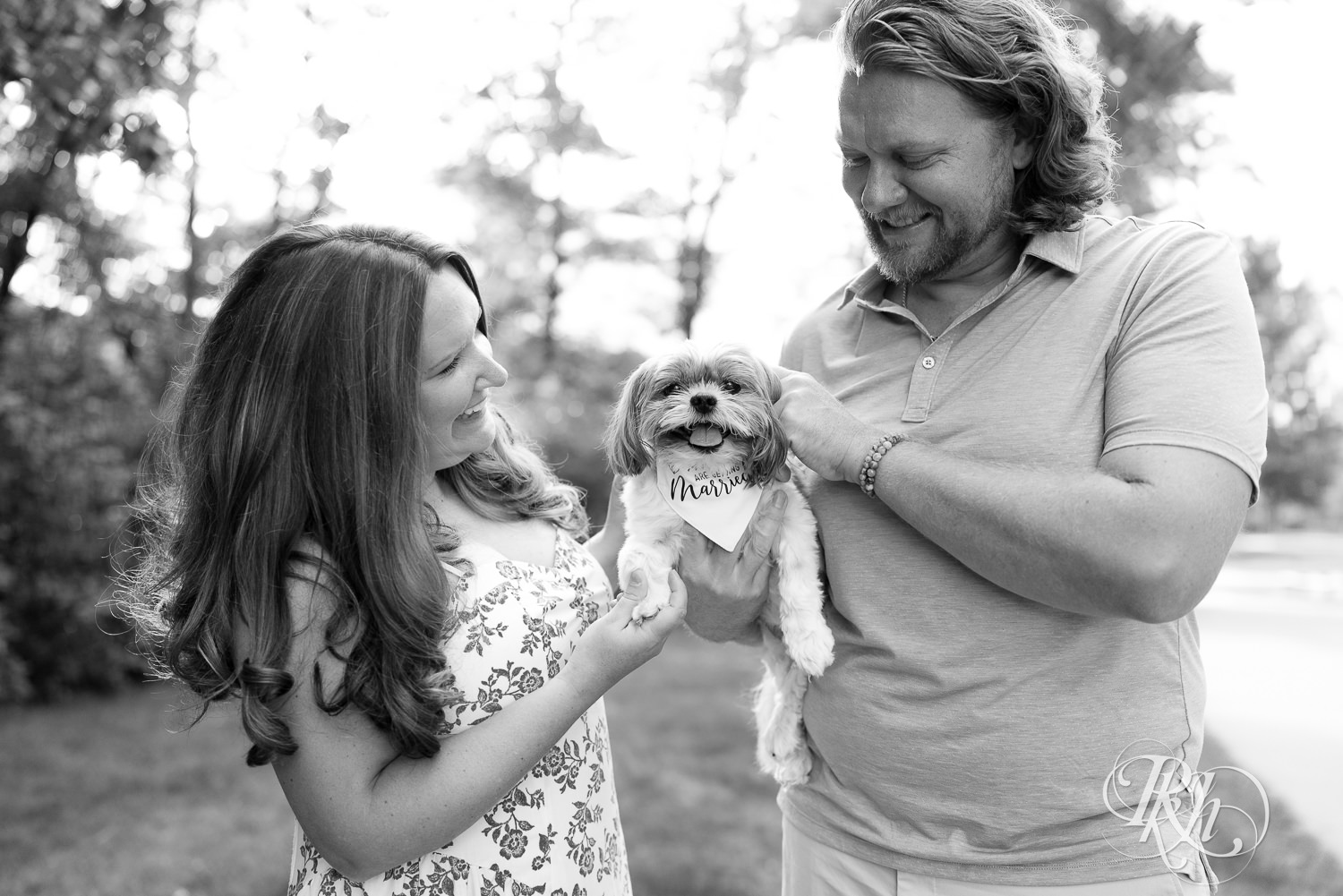 Man in blue shirt and khaki shorts and woman in blue and white dress smile while holding dog at sunset in Eagan, Minnesota.
