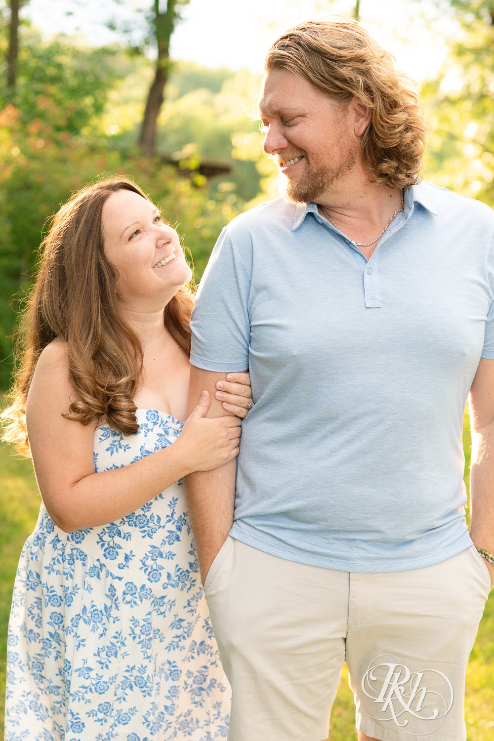 Man in blue shirt and khaki shorts and woman in blue and white dress smile at each other at sunset in Eagan, Minnesota.