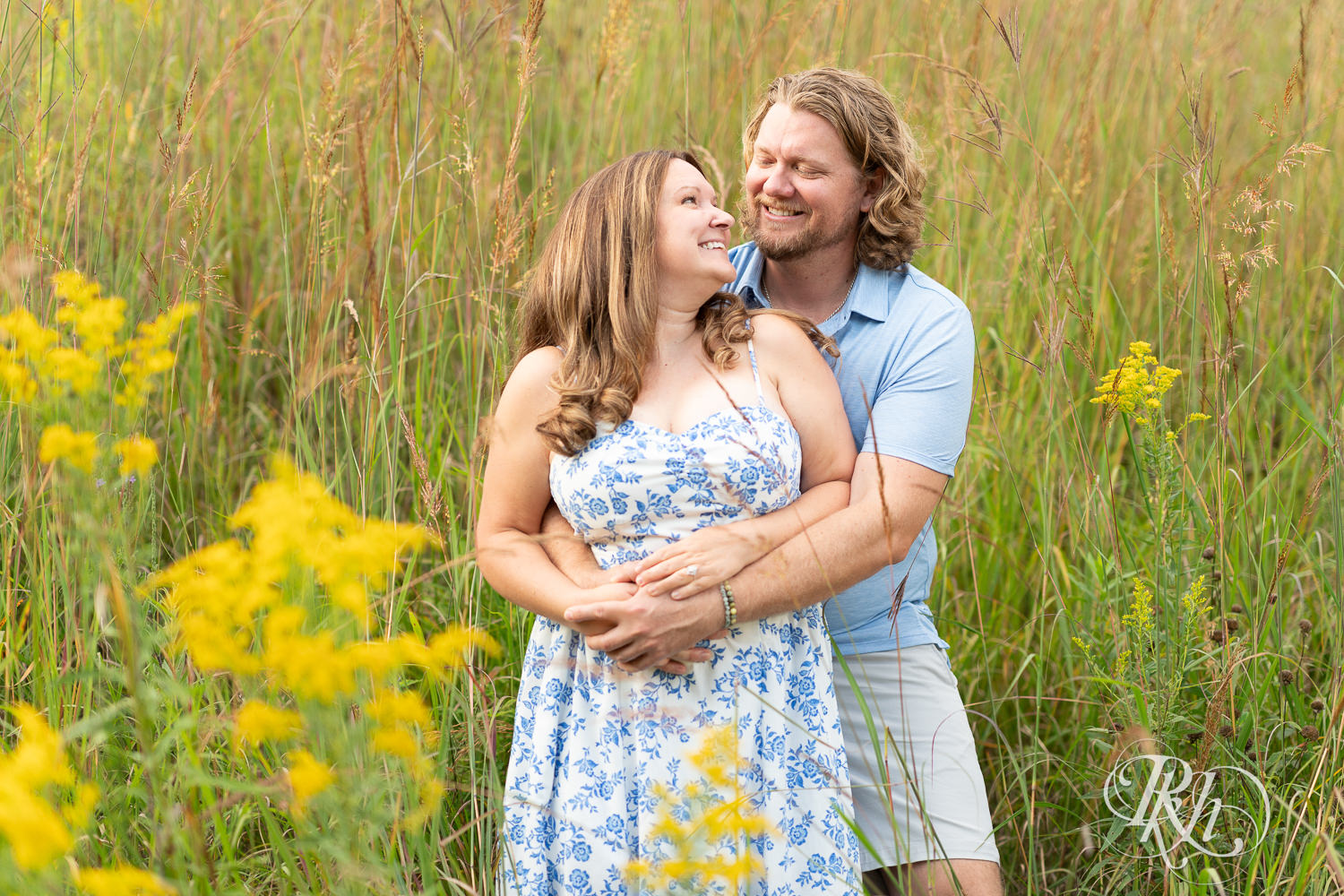 Man in blue shirt and khaki shorts and woman in blue and white dress smile within flowers in Eagan, Minnesota.