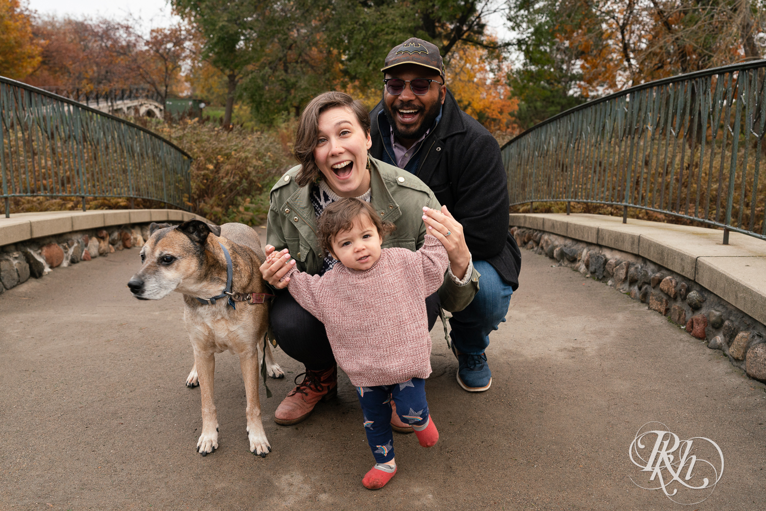 Man and woman smile with their daughter and dog on the bridge during a family photography session at Como Park in Saint Paul, Minnesota.