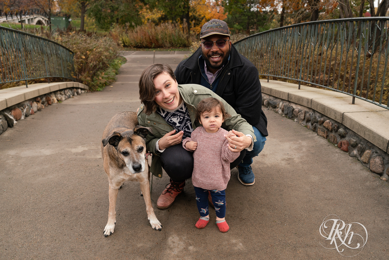 Man and woman smile with their daughter and dog on the bridge during a family photography session at Como Park in Saint Paul, Minnesota.