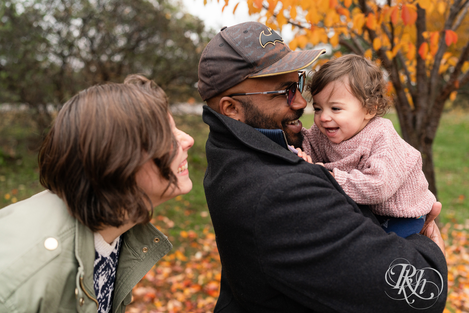 Little girl laughs while her parents play with her during a family photography session at Como Park in Saint Paul, Minnesota.