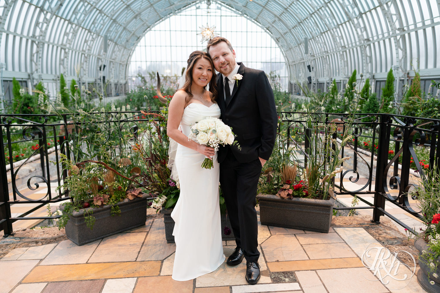 Asian bride and groom smile on wedding day at the Sunken Garden at the Como Zoo and Conservatory in Saint Paul, Minnesota.