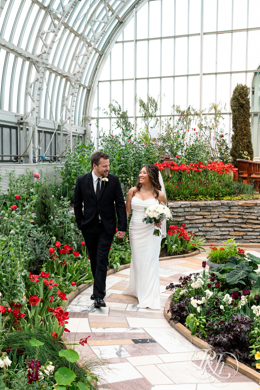 Asian bride and groom walk through flowers at the Sunken Garden at the Como Zoo and Conservatory in Saint Paul, Minnesota.