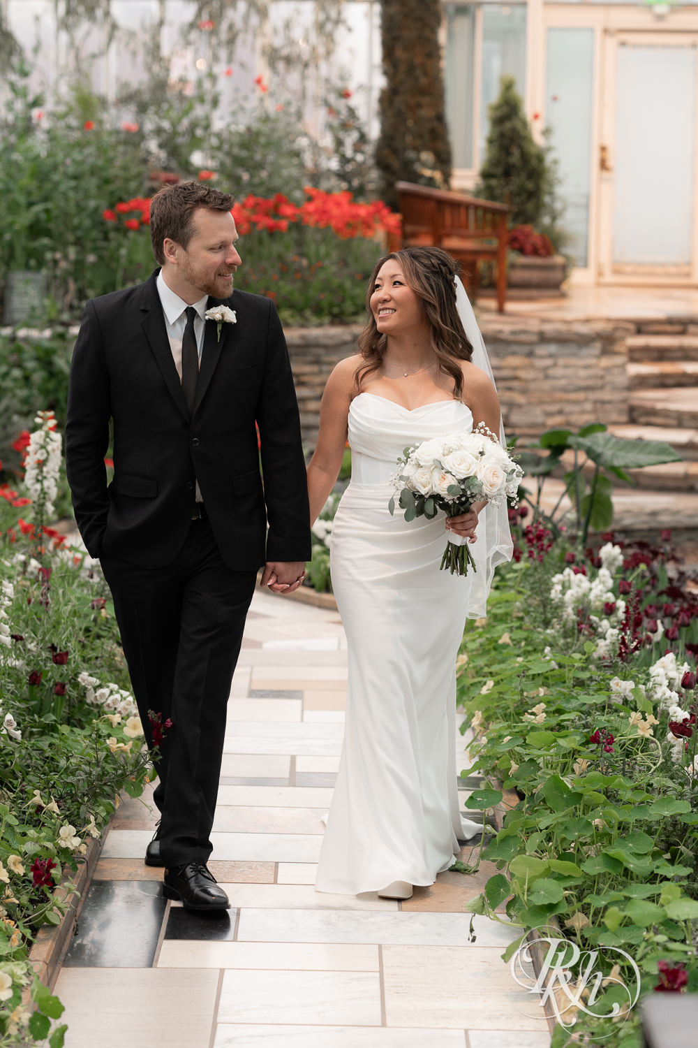 Asian bride and groom walk through flowers at the Sunken Garden at the Como Zoo and Conservatory in Saint Paul, Minnesota.