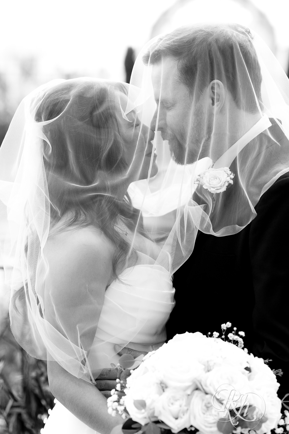 Asian bride and groom kiss under wedding veil at the Como Zoo and Conservatory in Saint Paul, Minnesota.