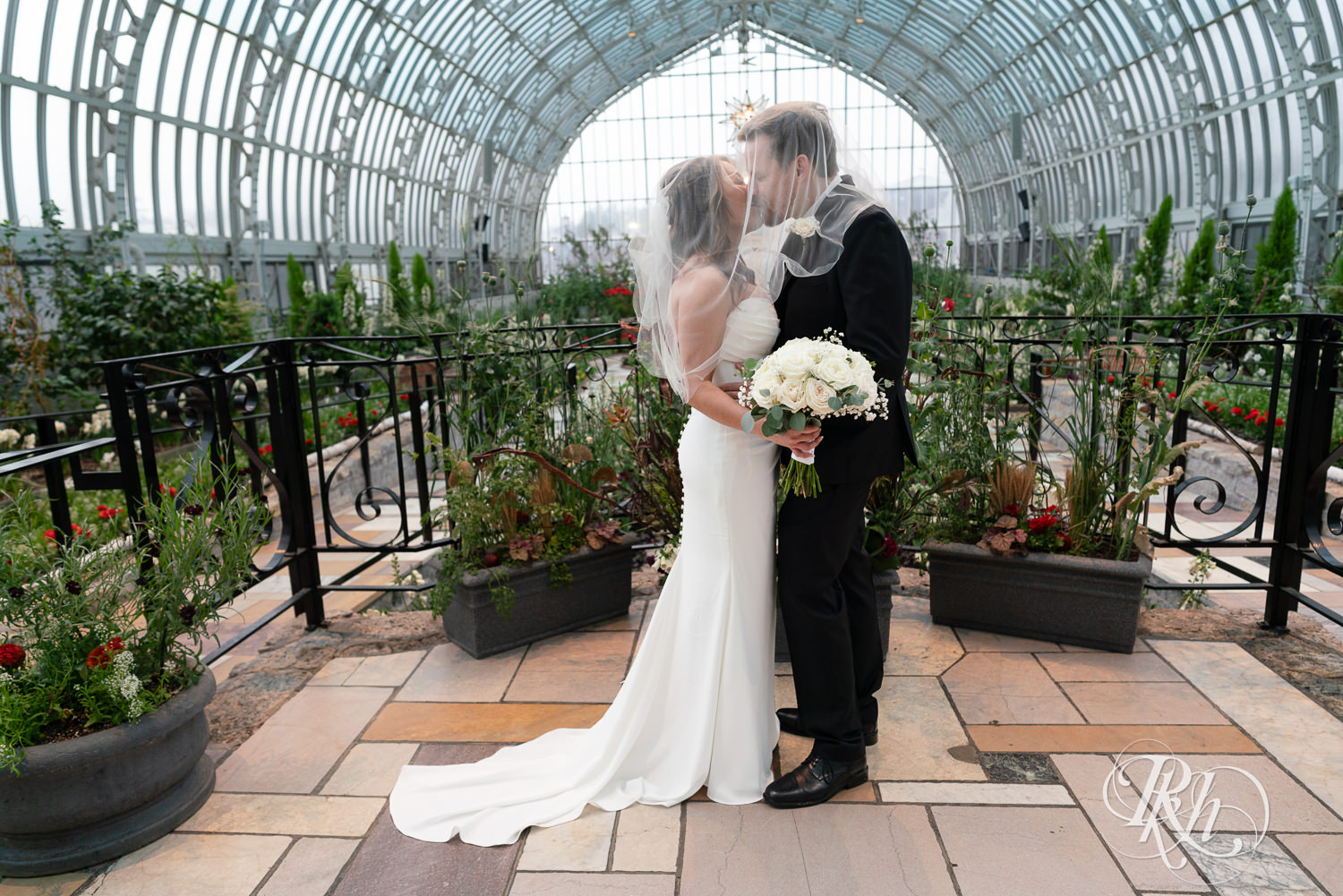 Asian bride and groom kiss under wedding veil at the Como Zoo and Conservatory in Saint Paul, Minnesota.
