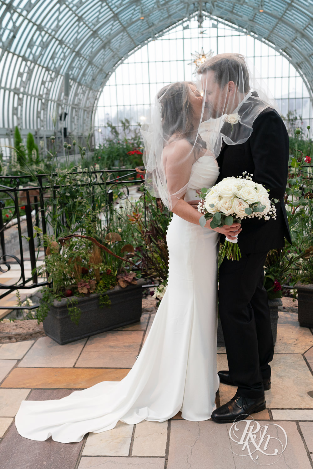 Asian bride and groom kiss under wedding veil at the Como Zoo and Conservatory in Saint Paul, Minnesota.