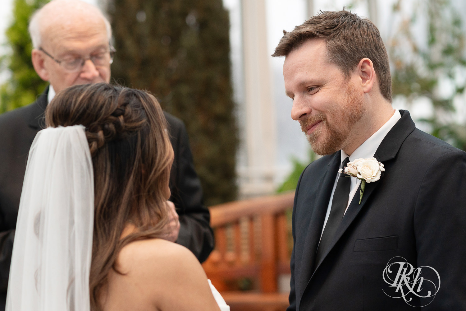 Groom smiles at bride during wedding ceremony in the Sunken Garden at the Como Zoo and Conservatory in Saint Paul, Minnesota.