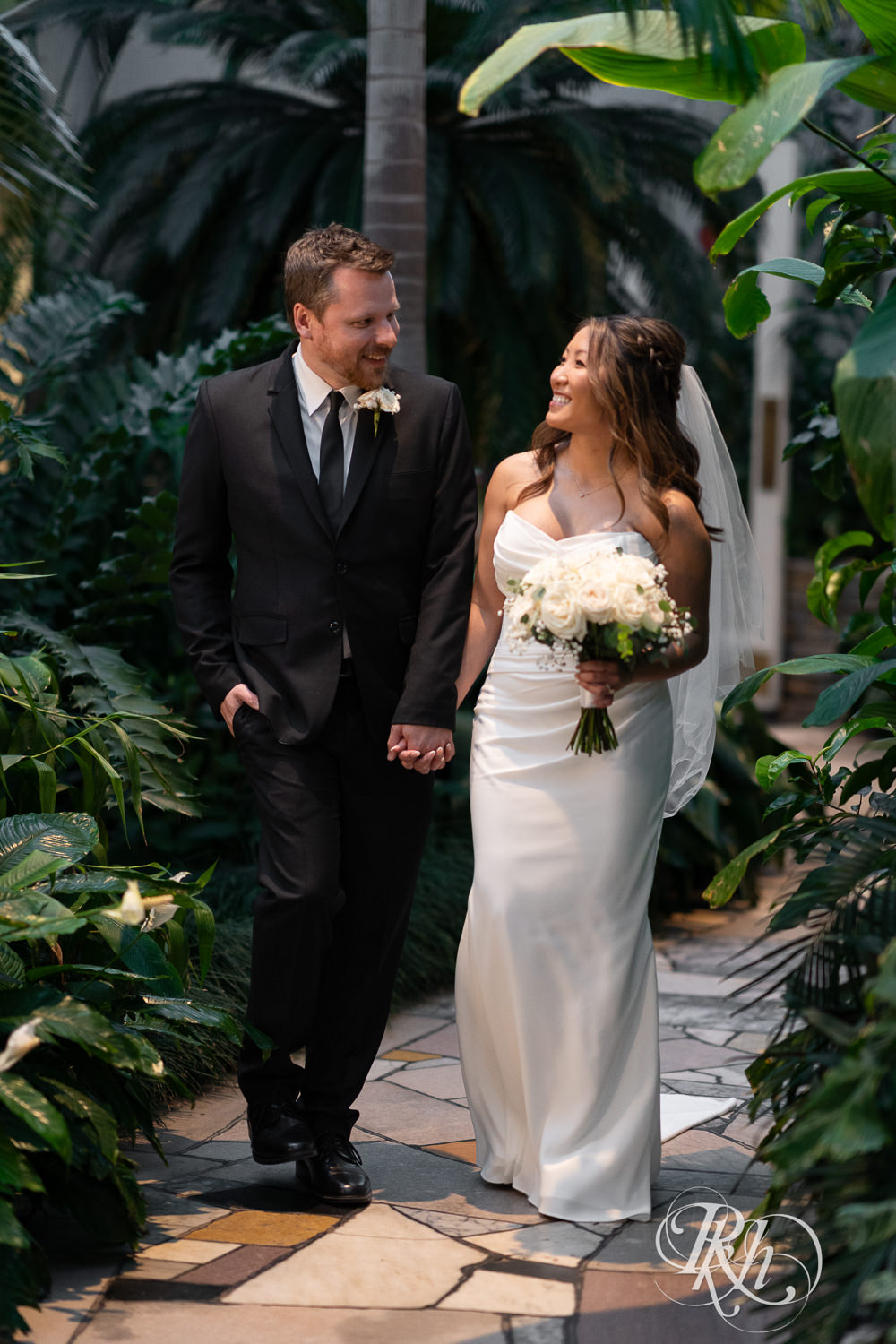 Asian bride and groom walk through the Palm Dome at the Como Zoo and Conservatory in Saint Paul, Minnesota.