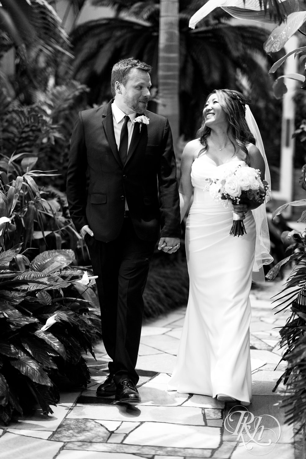 Asian bride and groom walk through the Palm Dome at the Como Zoo and Conservatory in Saint Paul, Minnesota.
