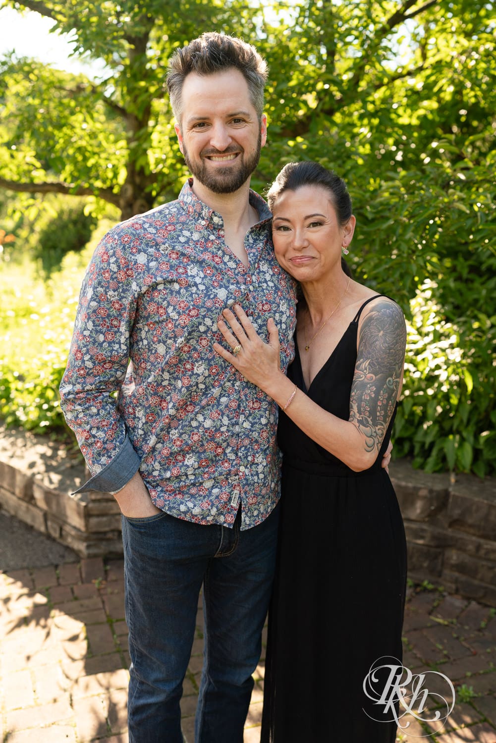 Man and woman in a black dress smile at the camera during their Minnesota Landscape Arboretum engagement photography session.