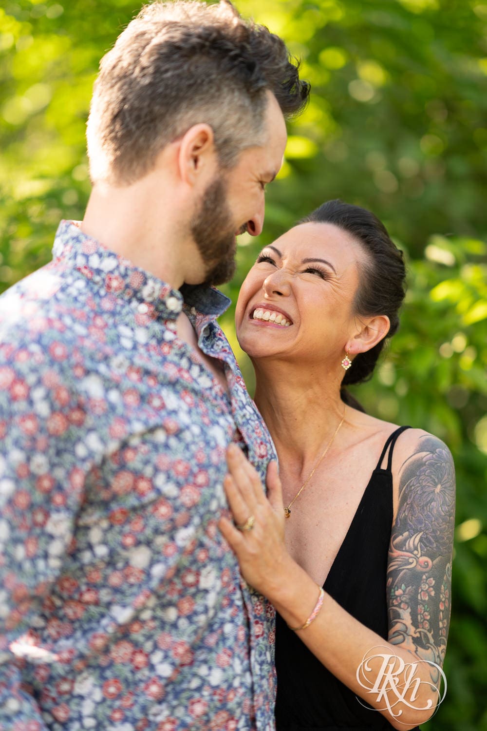Man and woman in a black dress smile at each other during their Minnesota Landscape Arboretum engagement photography session.