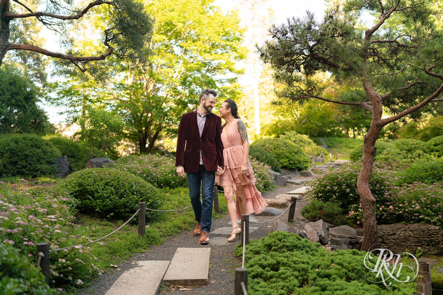 Man in red velvet jacket and a woman in a pink dress walk together at Minnesota Landscape Arboretum in Chaska, Minnesota.