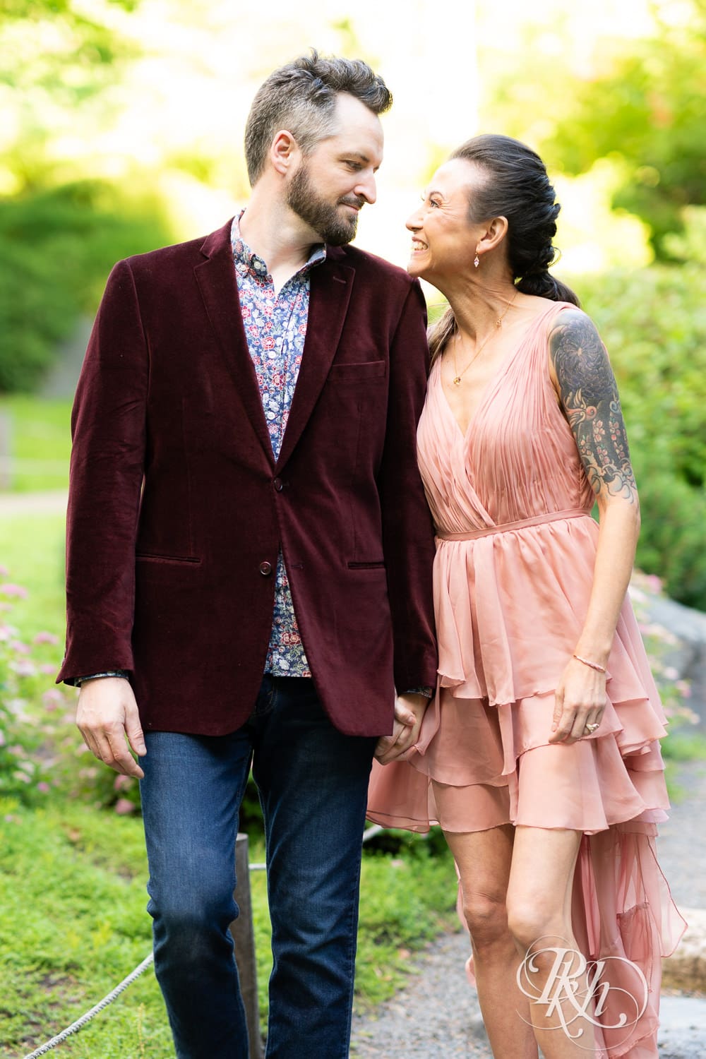 Man in red velvet jacket and a woman in a pink dress walk together at Minnesota Landscape Arboretum in Chaska, Minnesota.