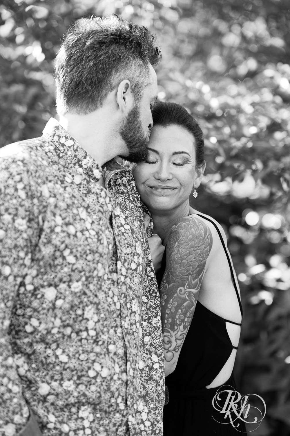 Man and woman in a black dress kiss during their Minnesota Landscape Arboretum engagement photography session.