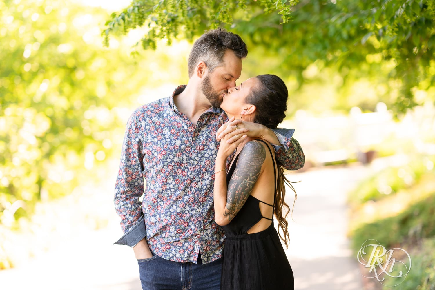 Man and woman in a black dress kiss during sunset at their Minnesota Landscape Arboretum engagement photography session.