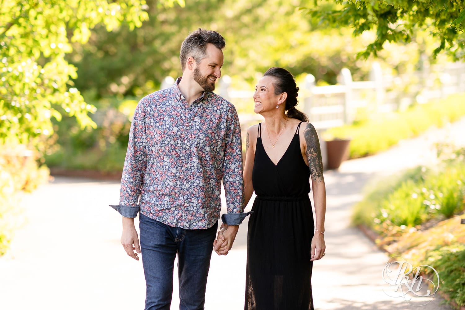 Man and woman in a black dress walk together during sunset at their Minnesota Landscape Arboretum engagement photography session.